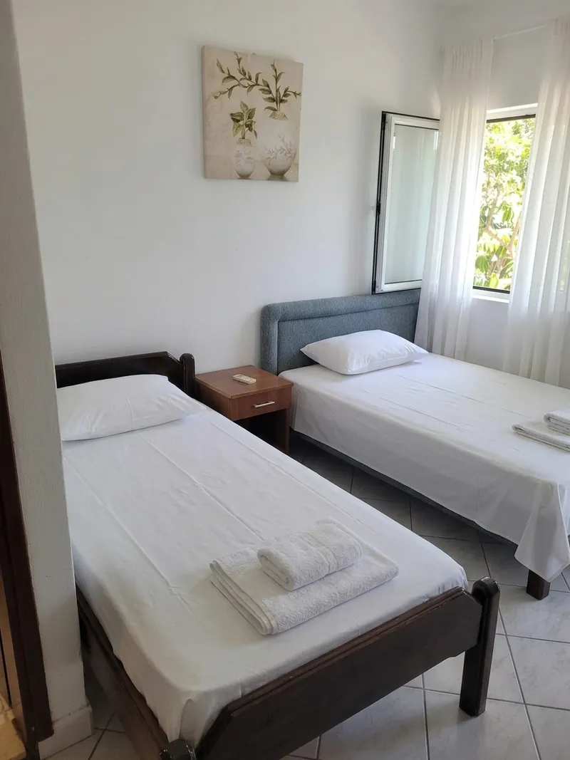 Two single beds with white linen, a bedside table and a window onto greenery